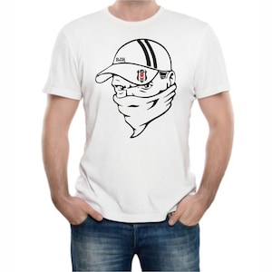 May include: White t-shirt featuring a black and white graphic of a person wearing a cap with the letters "BJK" and a face covering. The graphic has a bold, stylized design.