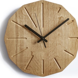 May include: A wooden wall clock with black hands and a unique octagonal shape. The clock face has a light wood grain and features a simple design with black hour markers.