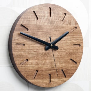 May include: A round wooden wall clock with black hands and a simple design. The clock face is made of natural wood with a grain pattern. The clock has a minimalist style and would look great in any modern home.