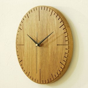 May include: A round wooden wall clock with black hands and a wood grain finish. The clock face has a simple design with black markings for the hours.