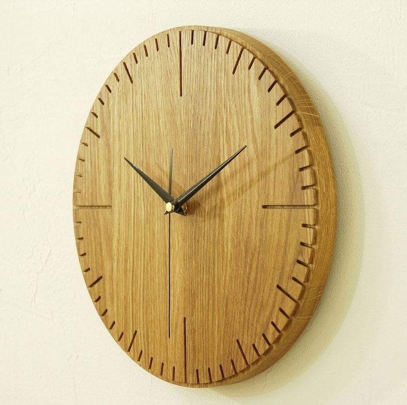 May include: A round wooden wall clock with black hands and a wood grain finish. The clock face has a simple design with black markings for the hours.