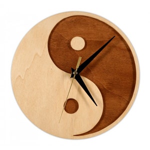 May include: A wooden wall clock with a yin yang design. The clock face is made of two different types of wood, one light and one dark. The hands of the clock are black and gold.