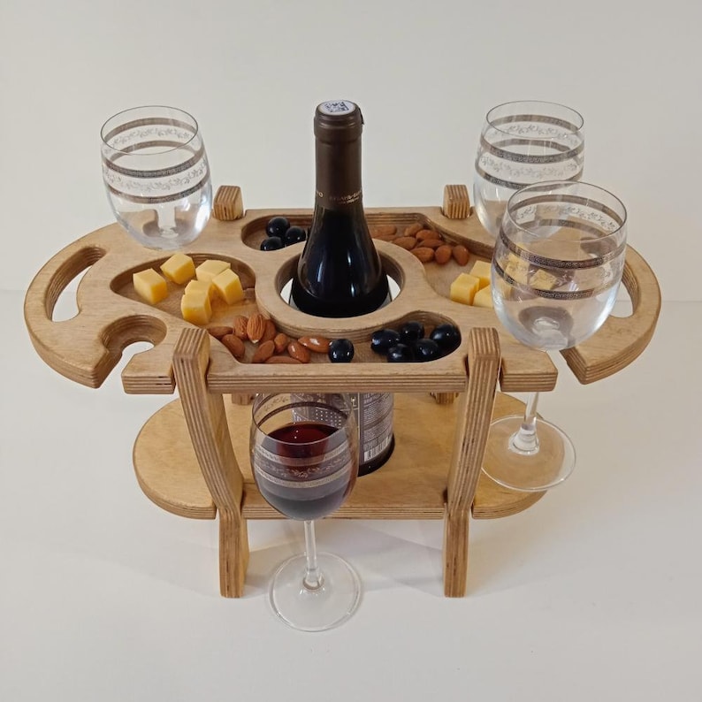 Puede incluir: Bandeja de servicio de madera para vino y queso de dos niveles. El nivel superior tiene cuatro vasos, una botella de vino y compartimentos para queso y almendras. El nivel inferior tiene un solo vaso.
