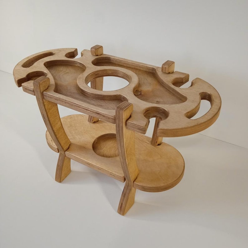 Puede incluir: Un soporte de madera con dos estantes, dise&ntilde;ado para sostener botellas y vasos. El estante superior tiene recortes para botellas y vasos, mientras que el estante inferior es una superficie plana. El soporte est&aacute; hecho de madera de color claro y tiene un acabado natural.