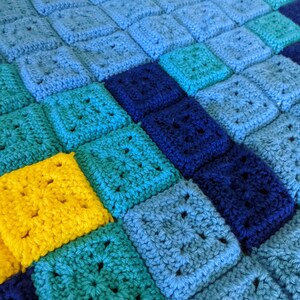 May include: A crocheted blanket with squares in shades of blue, teal, and yellow. The squares are arranged in a diagonal pattern.
