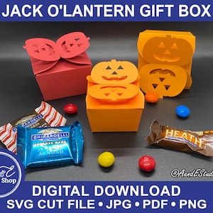 May include: A digital download SVG cut file for a Jack O' Lantern gift box. The image shows a three-dimensional orange and red box with a jack-o'-lantern face on each side. The box is sitting on a table with candy bars and other Halloween decorations.