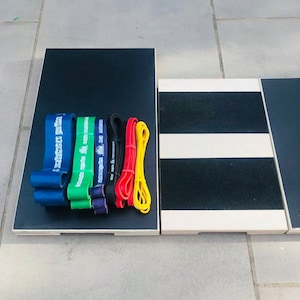 May include: A collection of resistance bands in blue, green, purple, black, red, and yellow, arranged on a black wooden platform. The bands are of varying thicknesses and lengths. Adjacent to the platform is a wooden step with black and white stripes.