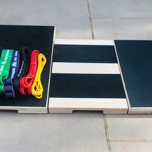 May include: A set of exercise equipment, including a black platform with a wooden frame, a center platform with black and white stripes, and a variety of resistance bands in blue, green, purple, black, red, and yellow. The bands are stacked on the platform.