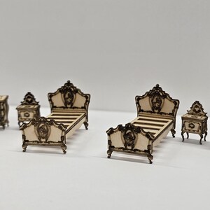 May include: A miniature bedroom set with a classic design. The set includes a chest of drawers, two bedside tables, two beds, and a tall cabinet. The furniture is light-coloured with dark brown trim and ornate details.