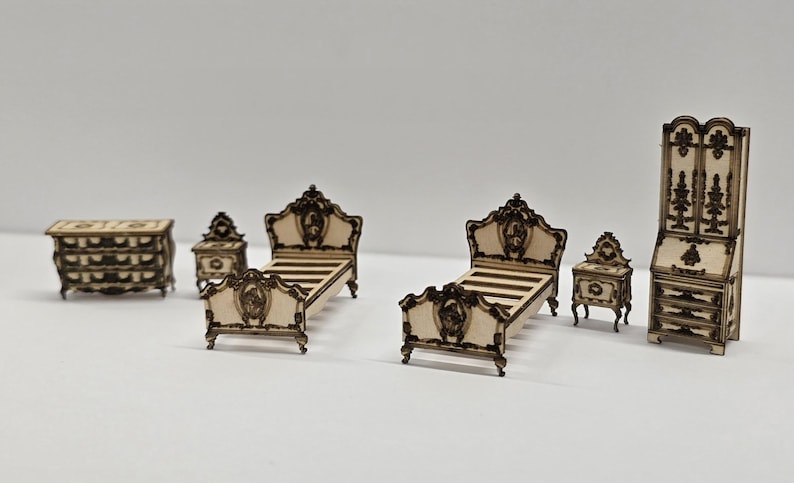May include: A miniature bedroom set with a classic design. The set includes a chest of drawers, two bedside tables, two beds, and a tall cabinet. The furniture is light-coloured with dark brown trim and ornate details.