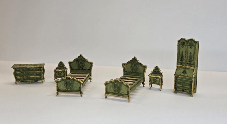 May include: Miniature bedroom furniture set in a classic style. The set includes a chest of drawers, two beds, two bedside tables, and a tall cabinet. The furniture is painted green with gold accents.