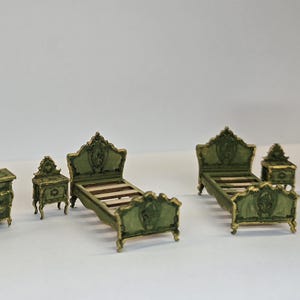 May include: A miniature bedroom set in a vintage style. The set includes a chest of drawers, two bedside tables, two beds, and a wardrobe. The furniture is painted dark green with gold accents, creating an antique aesthetic.