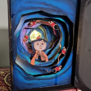 Pu&ograve; includere: Un'opera d'arte di libro pop-up 3D con una ragazza con gli occhi azzurri e un vestito rosso in piedi in un tunnel blu e oro vorticoso. Il tunnel &egrave; circondato da piccole figure rosse con le code.