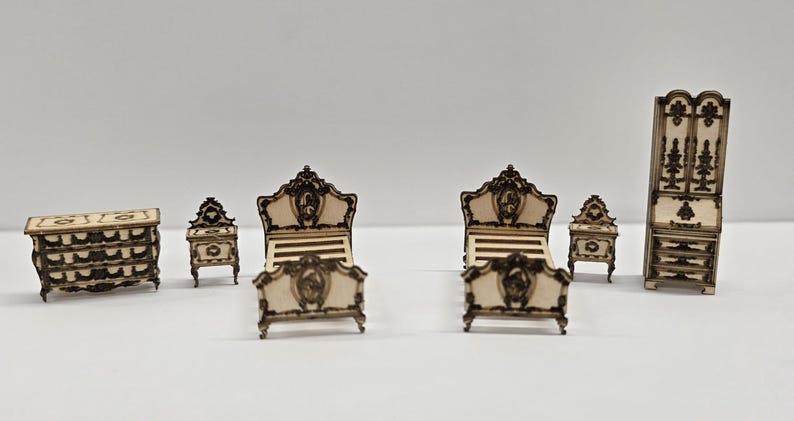 May include: Miniature bedroom furniture set. The set includes a chest of drawers, two bedside tables, two beds, and a wardrobe. The furniture is made of light-coloured wood with dark brown decorative accents. The bed frames have ornate headboards and footboards.