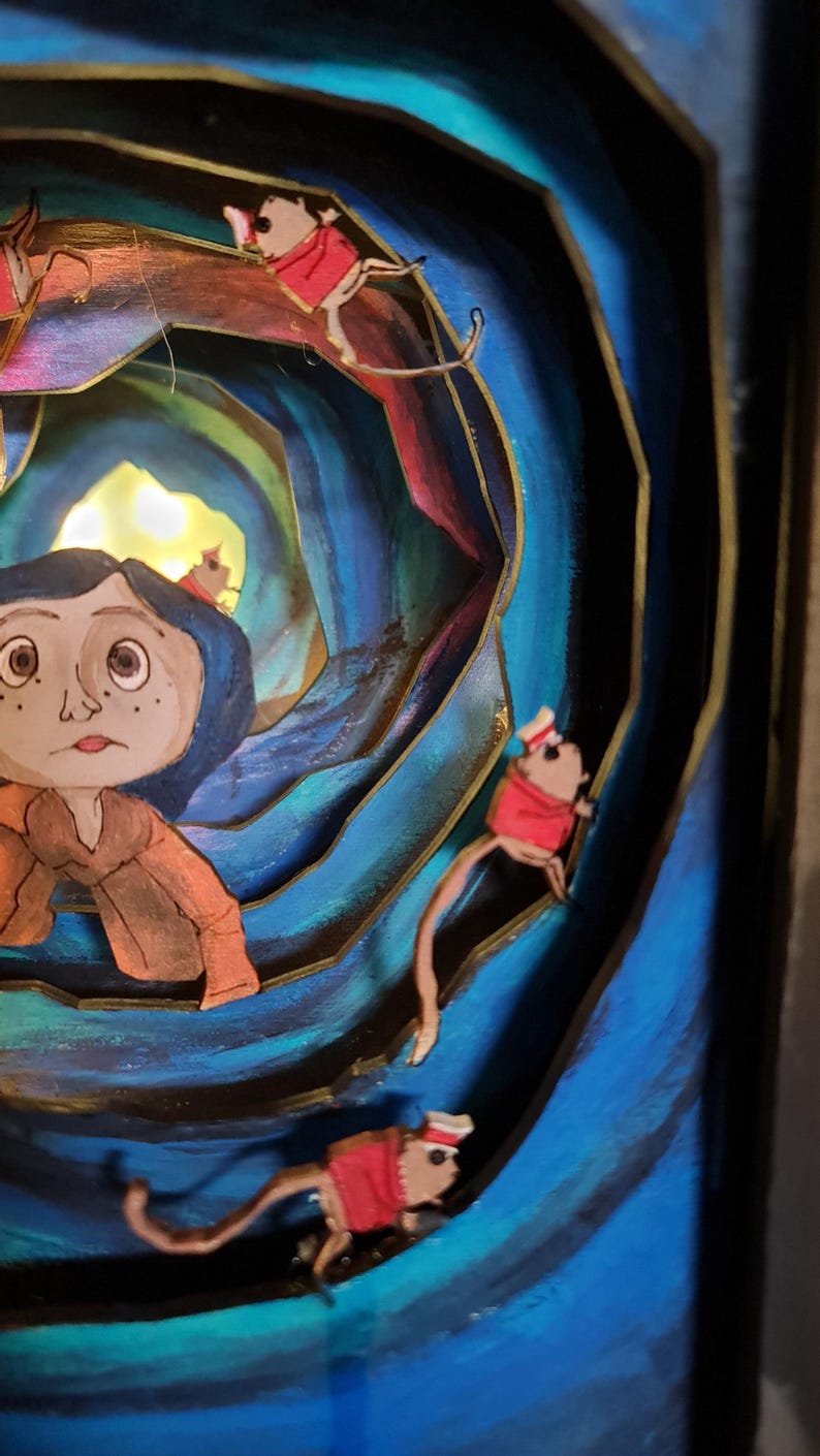 Pu&ograve; includere: Un diorama 3D di una ragazza con i capelli blu che guarda in un tunnel vorticoso con una luce alla fine. Il tunnel &egrave; fatto di legno dipinto di blu, verde e oro. Ci sono quattro piccoli topi con cappelli rossi e code che scalano le pareti del tunnel.