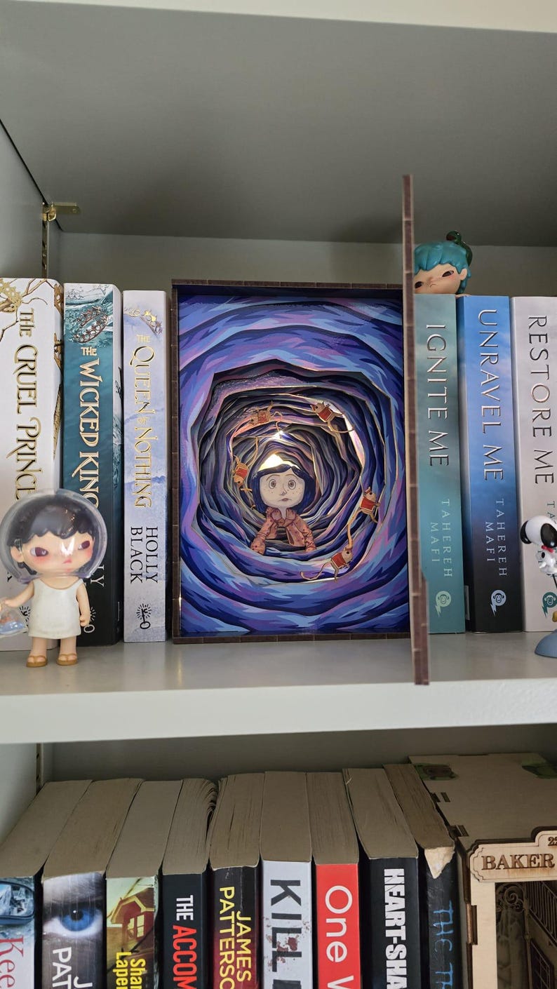 May include: A layered art piece depicting a girl in a tunnel with blue and purple hues. The artwork is displayed on a shelf with books and figurines. The books include titles like "The Cruel Prince" and "Queen Nothing".