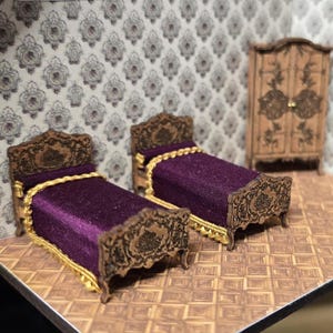 Puede incluir: Juego de dormitorio en miniatura con dos camas y un armario. Las camas tienen ropa de cama morada con ribetes dorados y marcos de madera ornamentados. El armario también es de madera con tallas decorativas. El papel pintado tiene un patrón floral repetido.