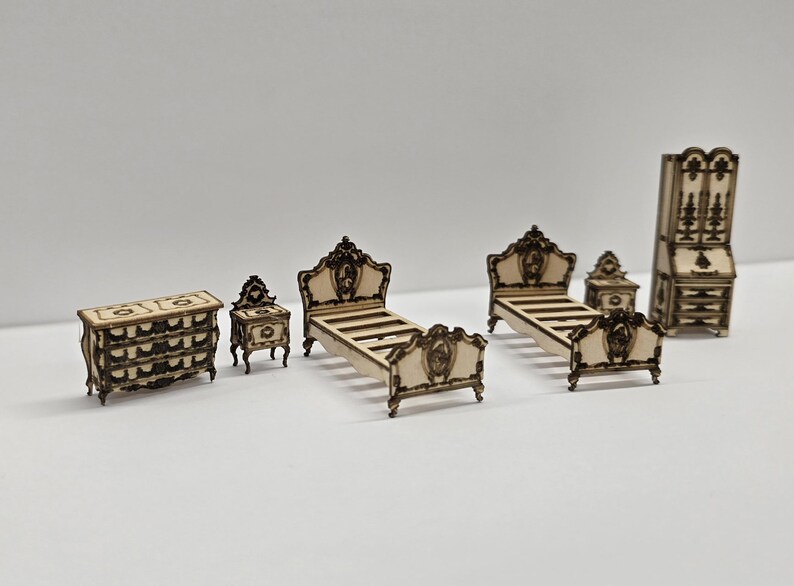 May include: A miniature bedroom furniture set, including a chest of drawers, two bedside tables, two beds, and a tall cabinet. The furniture is made of light-coloured wood with dark brown decorative accents. The beds have ornate headboards and footboards.