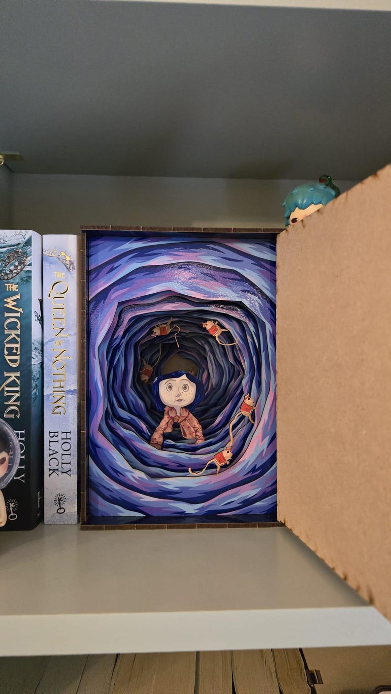 May include: A framed artwork depicting a young girl in a blue coat and hair, surrounded by a swirling tunnel of blue and purple hues. The artwork is displayed on a shelf with books.