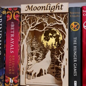 May include: A wooden bookend with a wolf howling at the moon in a forest scene. The bookend is labeled "Moonlight".