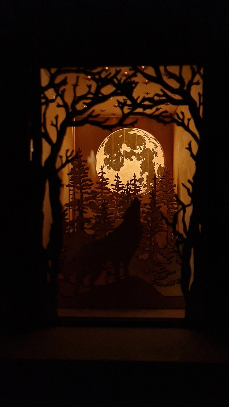 May include: A wooden silhouette of a wolf howling at the moon in a forest setting. The moon is full and illuminated, casting a warm glow on the scene. The wolf is silhouetted against the moon, and the trees are silhouetted against the moon and the wolf.