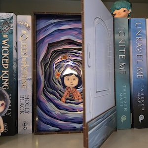 May include: A layered paper art piece depicting a scene from a fantasy story, featuring a character standing in a tunnel. The artwork is set against a backdrop of books on a shelf. The color palette includes blues, purples, and browns.