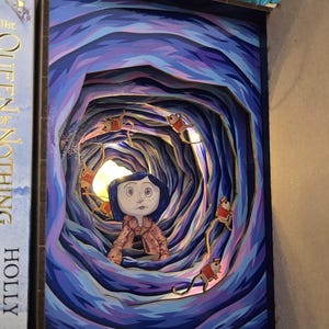 May include: A layered art piece depicting a scene from a movie. The artwork features a girl in a pink coat, surrounded by a swirling blue and purple tunnel. Small figures in red coats are suspended in the tunnel. The piece is framed in a dark blue border.