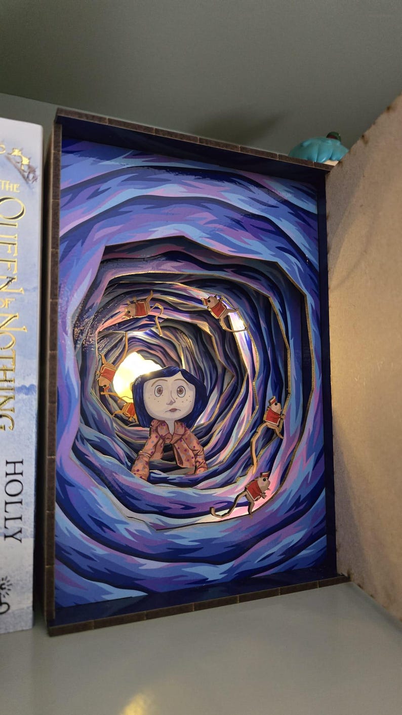May include: A layered art piece depicting a scene from a movie. The artwork features a girl in a pink coat, surrounded by a swirling blue and purple tunnel. Small figures in red coats are suspended in the tunnel. The piece is framed in a dark blue border.