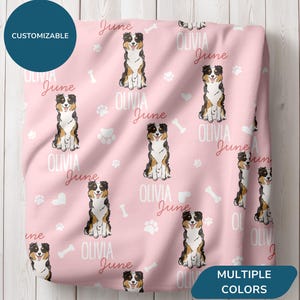 May include: Pink blanket featuring a repeating pattern of Australian Shepherd illustrations, paw prints, bones, and the names "Olivia" and "June". The blanket has a customizable design and is available in multiple colors.