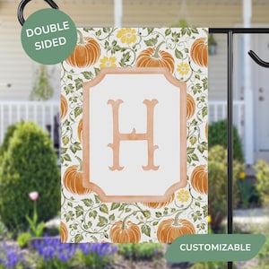 May include: Double-sided garden flag featuring a pumpkin and floral pattern with the letter "H" in a decorative frame. The flag has a white background and is accented with orange, yellow, and green colors. The word "CUSTOMIZABLE" is visible.