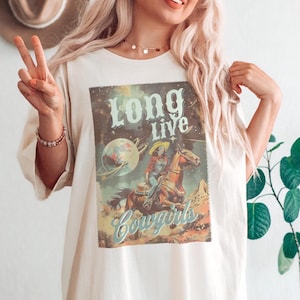 May include: A white oversized t-shirt with a vintage graphic print of a cowboy riding a horse. The graphic says "Long Live Cowgirls".