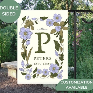 May include: A white garden flag with a floral wreath design. The wreath is made up of green leaves and purple flowers. In the center of the wreath is a large green letter "P" with the text "The Peters Est. 2025" below it.