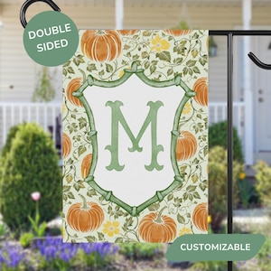 May include: Double-sided garden flag featuring a fall pumpkin pattern with a white shield and the letter "M" in green. The flag is displayed on a black metal stand and has the word "CUSTOMIZABLE" on the bottom.