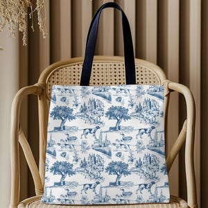 May include: A white tote bag with a blue and white toile pattern featuring a repeating design of trees, houses, and dogs. The bag has navy blue handles.