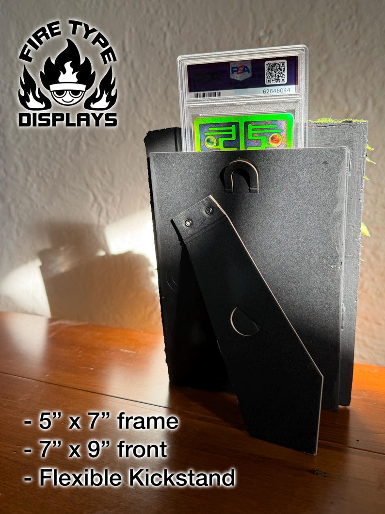 May include: A black display frame with a flexible kickstand, holding a PSA graded trading card in a clear plastic case. The frame features a 5 inch by 7 inch interior and a 7 inch by 9 inch front. The Fire Type Displays logo is visible in the corner.