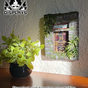 May include: A rectangular wall display featuring a stone-textured frame with green foliage accents. It holds a graded Ancient Mew Pok&eacute;mon card in a plastic slab. The display includes the text FIRE TYPE DISPLAYS and Standard wall hanging capabilities.