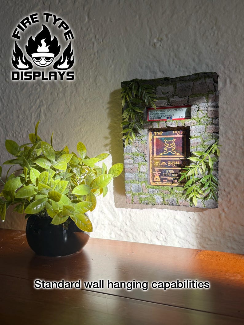May include: A rectangular wall display featuring a stone-textured frame with green foliage accents. It holds a graded Ancient Mew Pok&eacute;mon card in a plastic slab. The display includes the text FIRE TYPE DISPLAYS and Standard wall hanging capabilities.