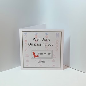 May include: A white card with a pink and grey border. The card has a red L on it and the text "Well Done On passing your Theory Test Jamie".