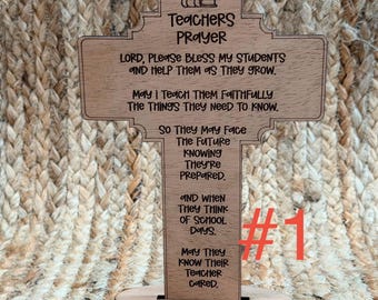 May include: Wooden cross-shaped plaque with the text "Teachers Prayer" and a prayer for students. The plaque features an apple and books icon at the top. The number "1" is visible on the right side.