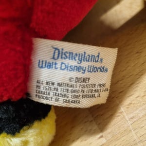 May include: A red and black plush toy with a yellow accent. The toy has a tag that reads "Disneyland Walt Disney World&reg;" and "&copy; Disney All new materials polyester fibers.  Made in China.  SR 1325-PA 1178-MASS 7-419.  Canasa Trading Corp. Burbank, CA.  Product of Sri Lanka."