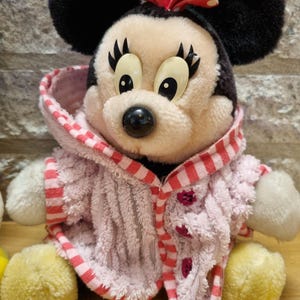 May include: A plush toy of Mickey Mouse wearing a pink and red striped robe. The toy has black ears, a red bow with white polka dots, and large black eyes.