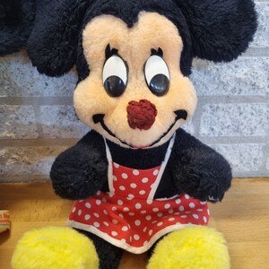 May include: A plush toy of Minnie Mouse wearing a red and white polka dot dress and a red bow. She has large black eyes and a red nose.