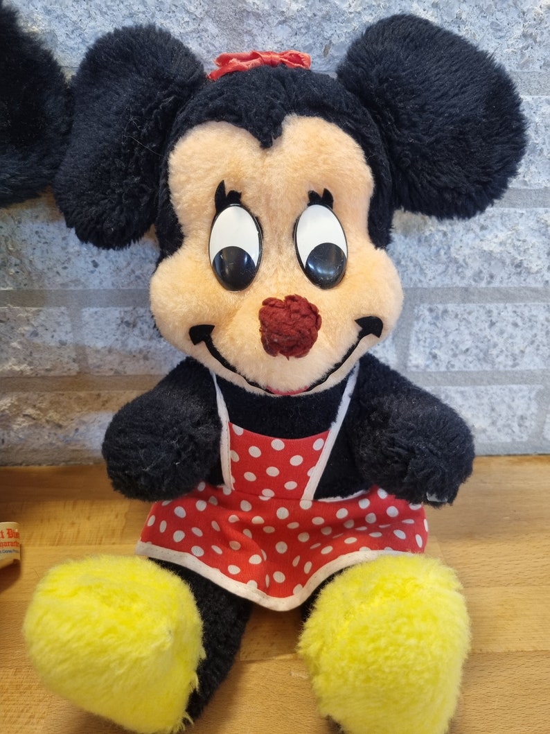 May include: A plush toy of Minnie Mouse wearing a red and white polka dot dress and a red bow. She has large black eyes and a red nose.