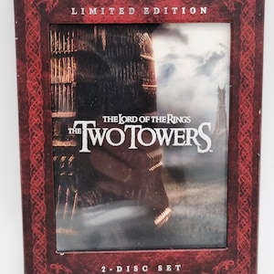 Può includere: Un cofanetto DVD in edizione limitata de "Il Signore degli Anelli: Le Due Torri". La scatola è rosso scuro con bordi decorativi e il titolo del film ben in evidenza. La copertina presenta una scena del film.