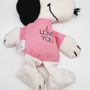 May include: A pink and white plush toy of Snoopy wearing a pink shirt with the text "I LOVE YOU".