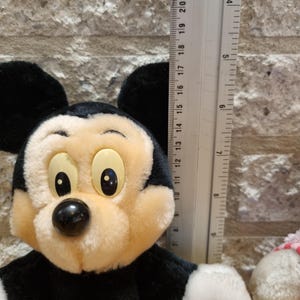 May include: A plush Mickey Mouse toy with black ears, a black nose, and large yellow eyes. The toy is wearing red shorts with yellow buttons. The toy is approximately 11 inches tall.