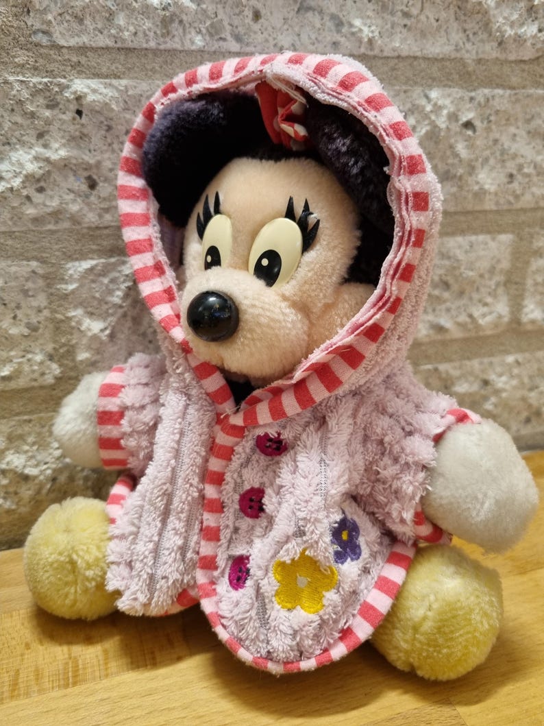 May include: A plush pink and red striped hooded robe with embroidered flowers, worn by a plush Mickey Mouse character.
