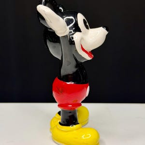 K&ouml;nnte beinhalten: Eine Keramikfigur von Mickey Mouse, mit schwarzem K&ouml;rper, wei&szlig;en Handschuhen und Gesicht, roter Hose und gelben Schuhen. Die Figur ist in Seitenansicht dargestellt, mit einem l&auml;chelnden Gesichtsausdruck.