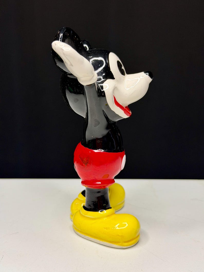 K&ouml;nnte beinhalten: Eine Keramikfigur von Mickey Mouse, mit schwarzem K&ouml;rper, wei&szlig;en Handschuhen und Gesicht, roter Hose und gelben Schuhen. Die Figur ist in Seitenansicht dargestellt, mit einem l&auml;chelnden Gesichtsausdruck.
