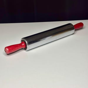 Peut inclure: Un rouleau à pâtisserie chromé avec des poignées en bois rouges. Cet ustensile de cuisine est conçu pour aplatir la pâte et d'autres tâches de pâtisserie. Le rouleau à pâtisserie mesure environ 30 cm de long.